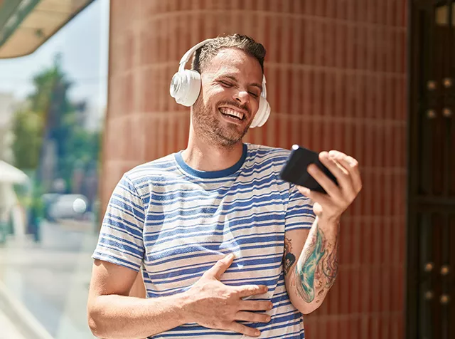 Un ragazzo sorridendo guarda lo smartphone simboleggiando la facilità con cui gli utilizzatori trovano i locali convenzionati sull’App