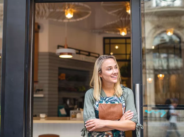 Immagine di un esercente che sorride davanti al suo negozio. Rappresenta i vantaggi e le opportunità di business che le soluzioni Pluxee apportano ai nostri partner commerciali.