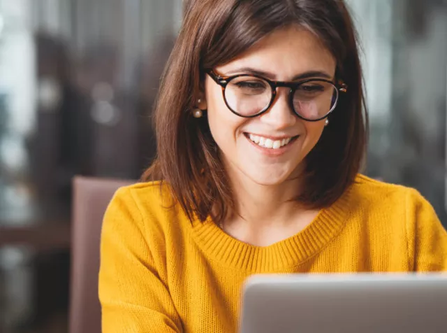 Immagine di una ragazza che sorride al pc. Rappresenta il mondo di opportunità che noi di Pluxee apriamo ai nostri partner commerciali.